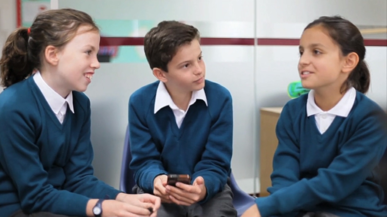 Primary pupils in blue uniform sit opposite each other discussing