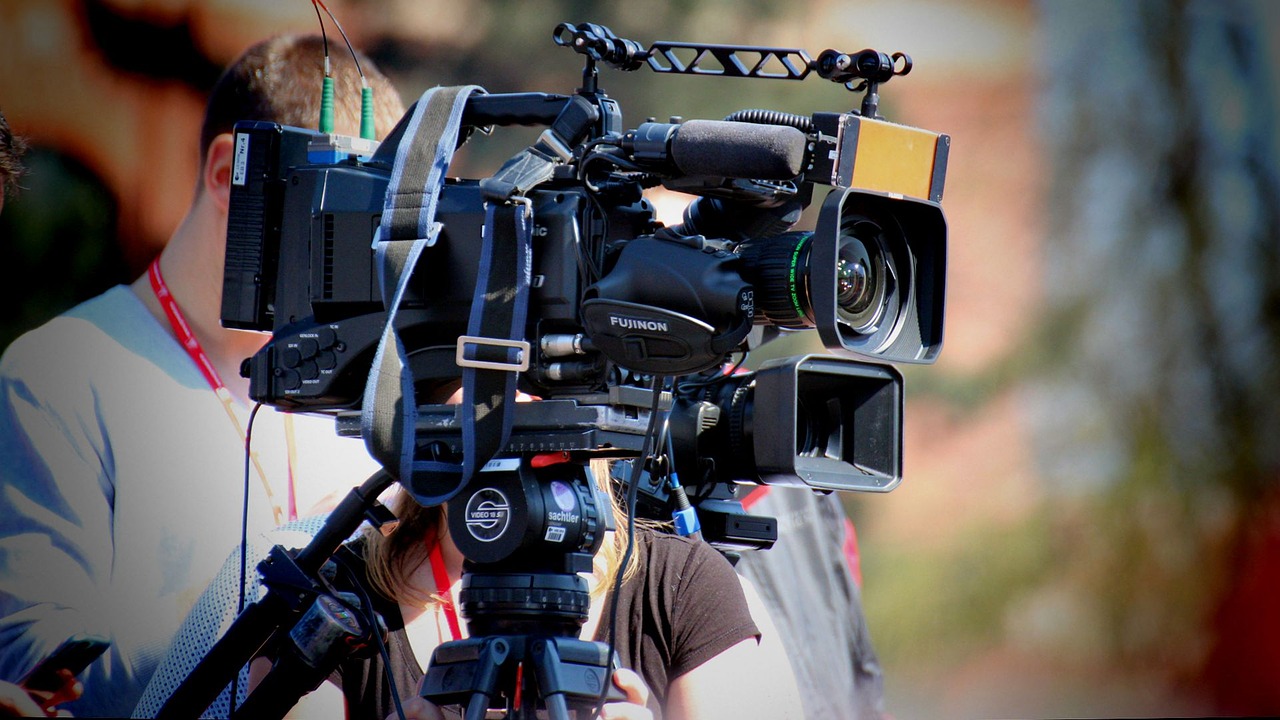 A student stands behind large camera filming equipment