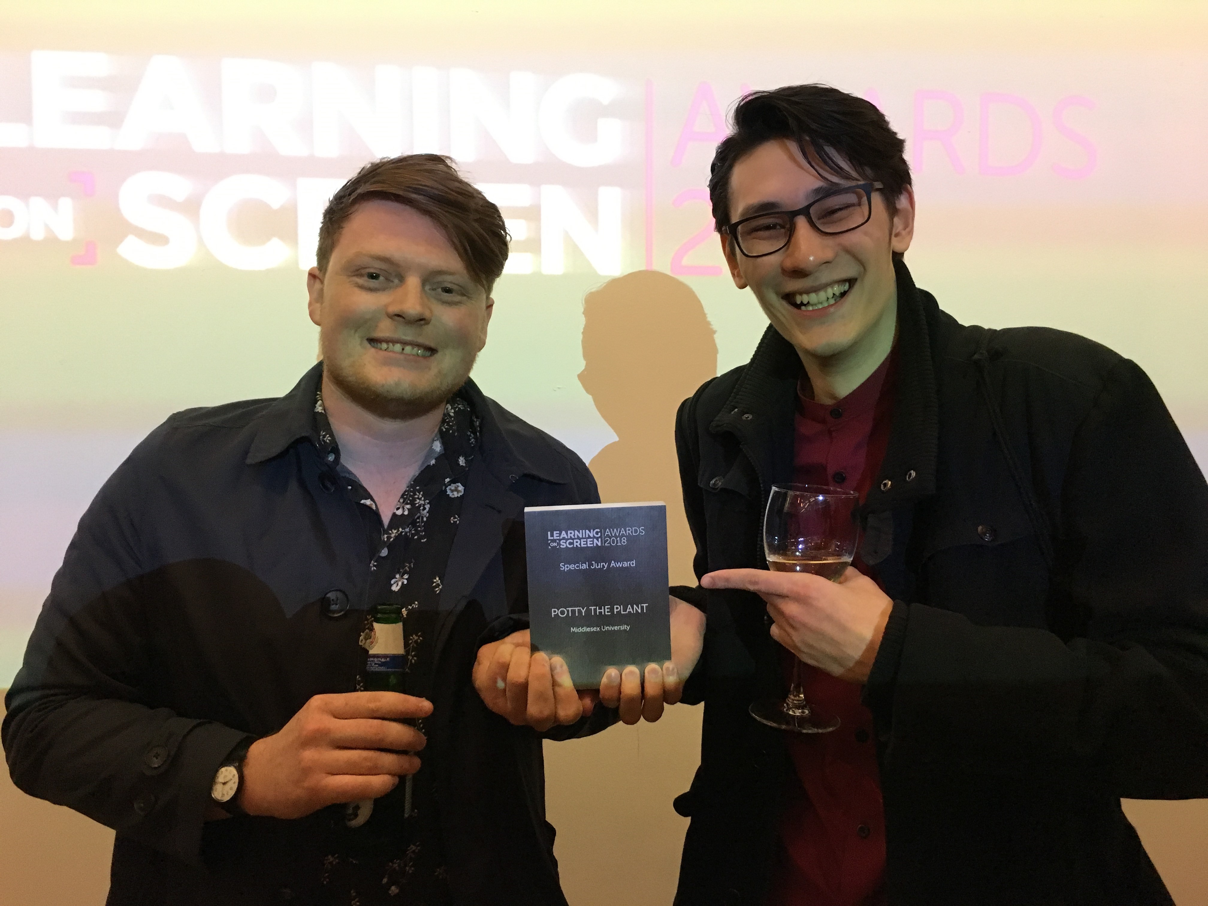 Two men at an award ceremony hold up their prize.